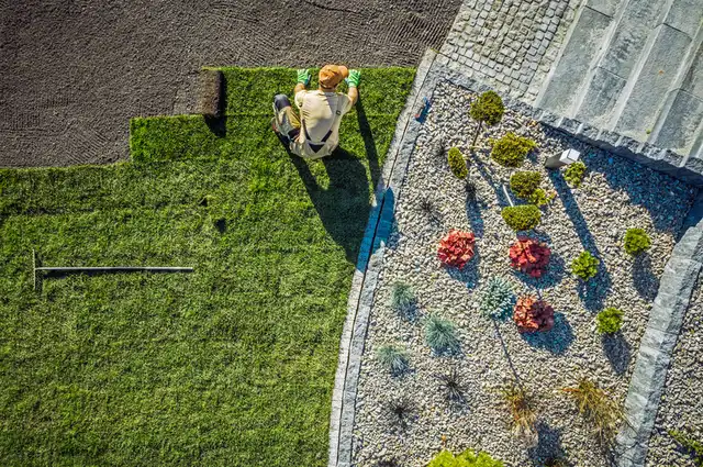 Laying fresh grass turf sod next to a pebble garden bed