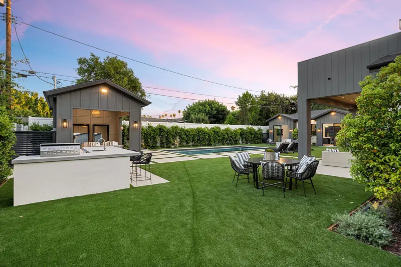 Luxurious backyard remodel with artificial turf, dining table, and swimming pool.